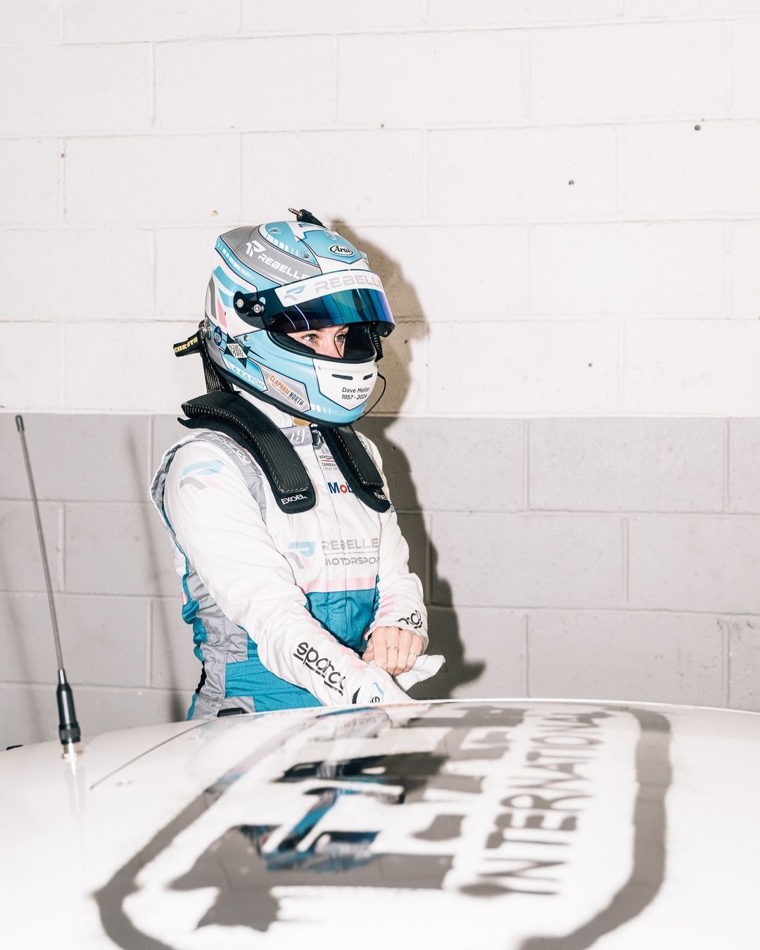 Abbie Eaton, CEO of Rebelleo Motorsport, prepares for racing by pulling on a glove. Her visor is open and eyes gaze forward with a sharp focus.