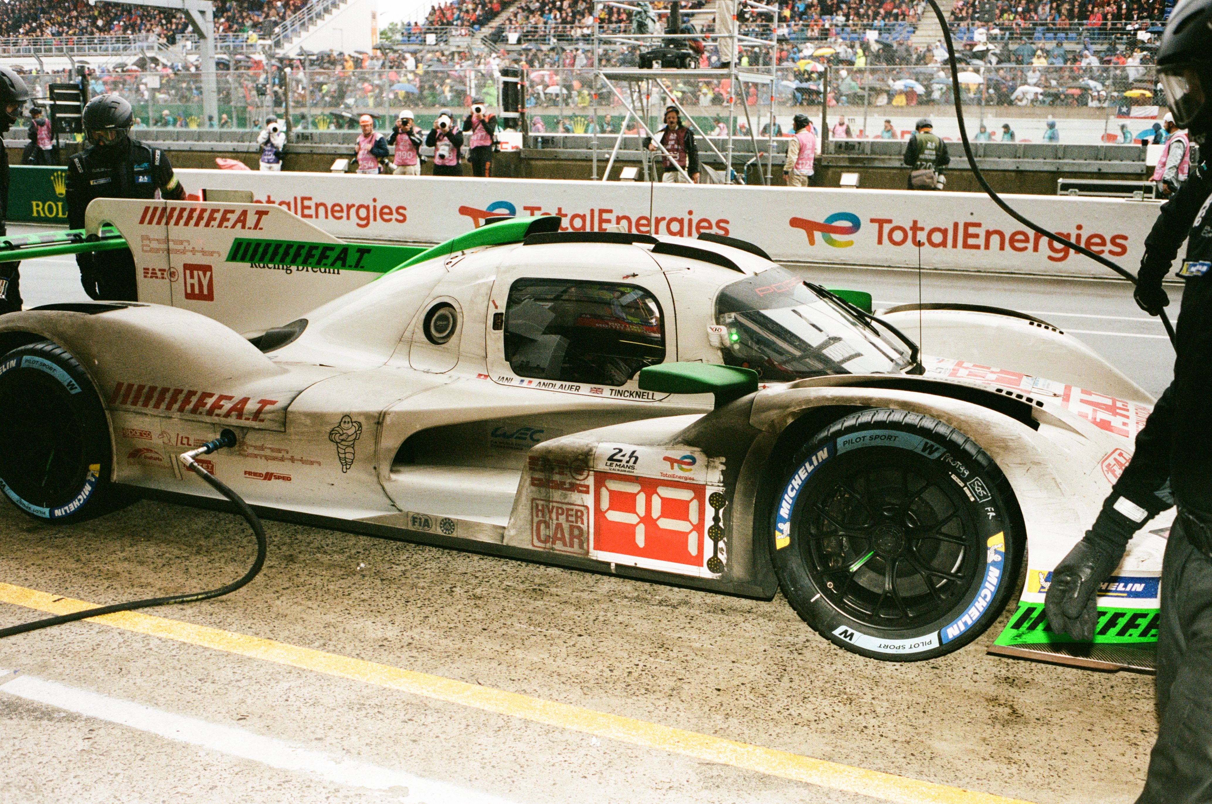 Hypercar #99 refueling in the pit lane with significant dirt and grime over the wheel wells from weather throughout the night time laps