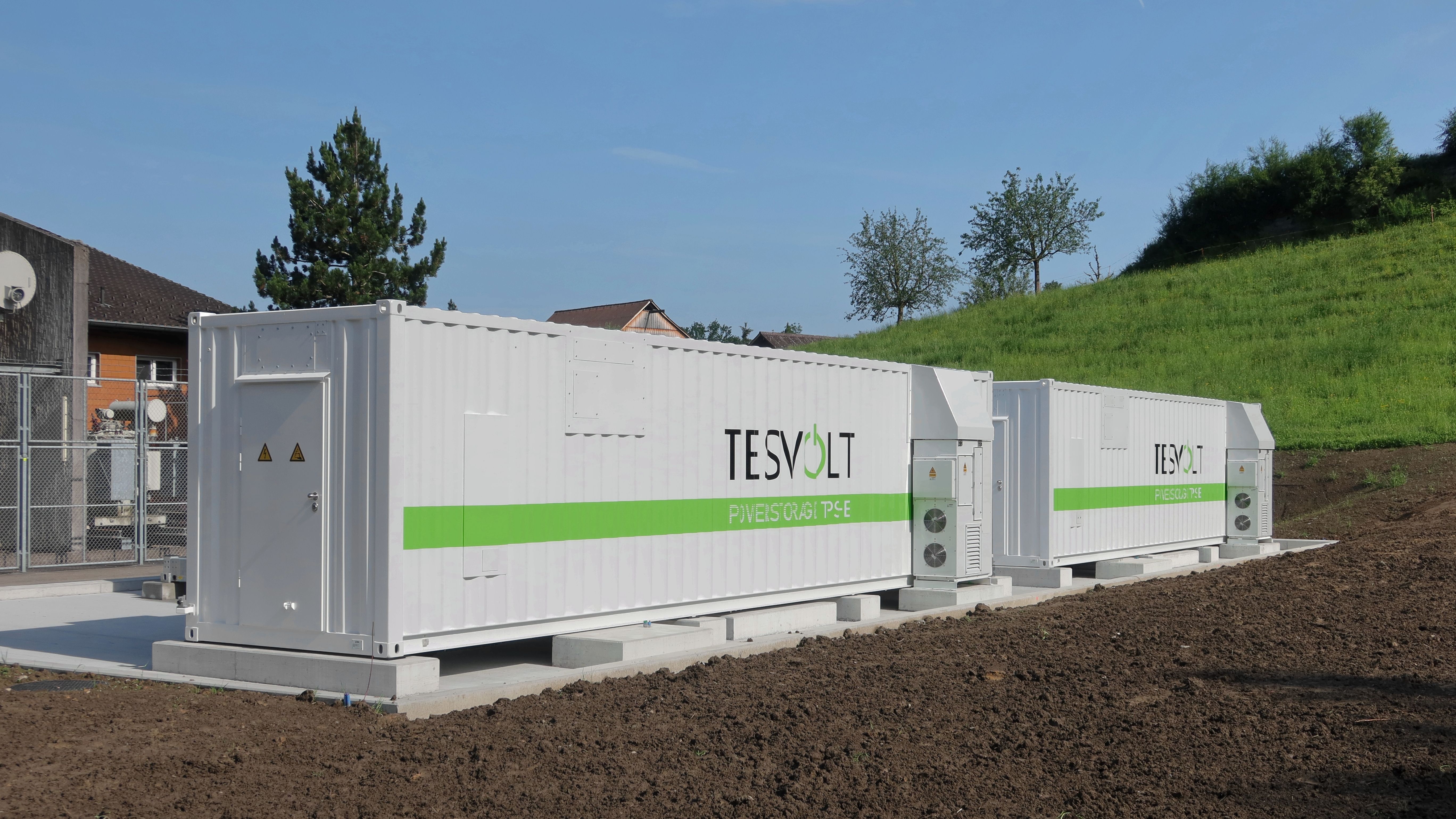 Dos contenedores blancos de un sistema de almacenamiento de energía en baterías junto a un edificio industrial