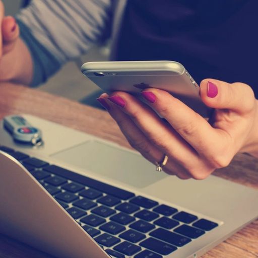 a woman is sitting at a table using a laptop and a cell phone .