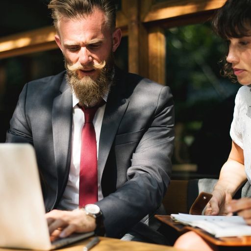 a man and a woman are sitting at a table looking at a laptop computer .