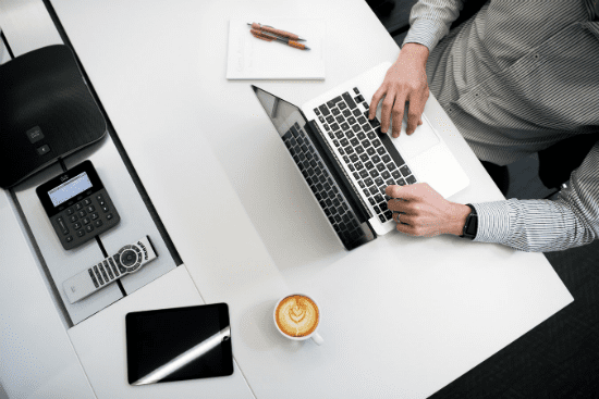 a man is typing on a laptop next to a cup of coffee