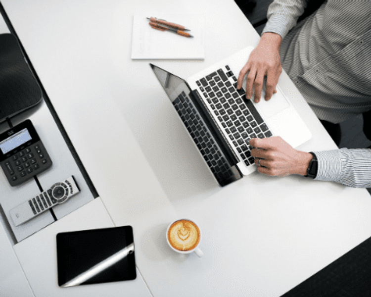 a man is typing on a laptop next to a cup of coffee