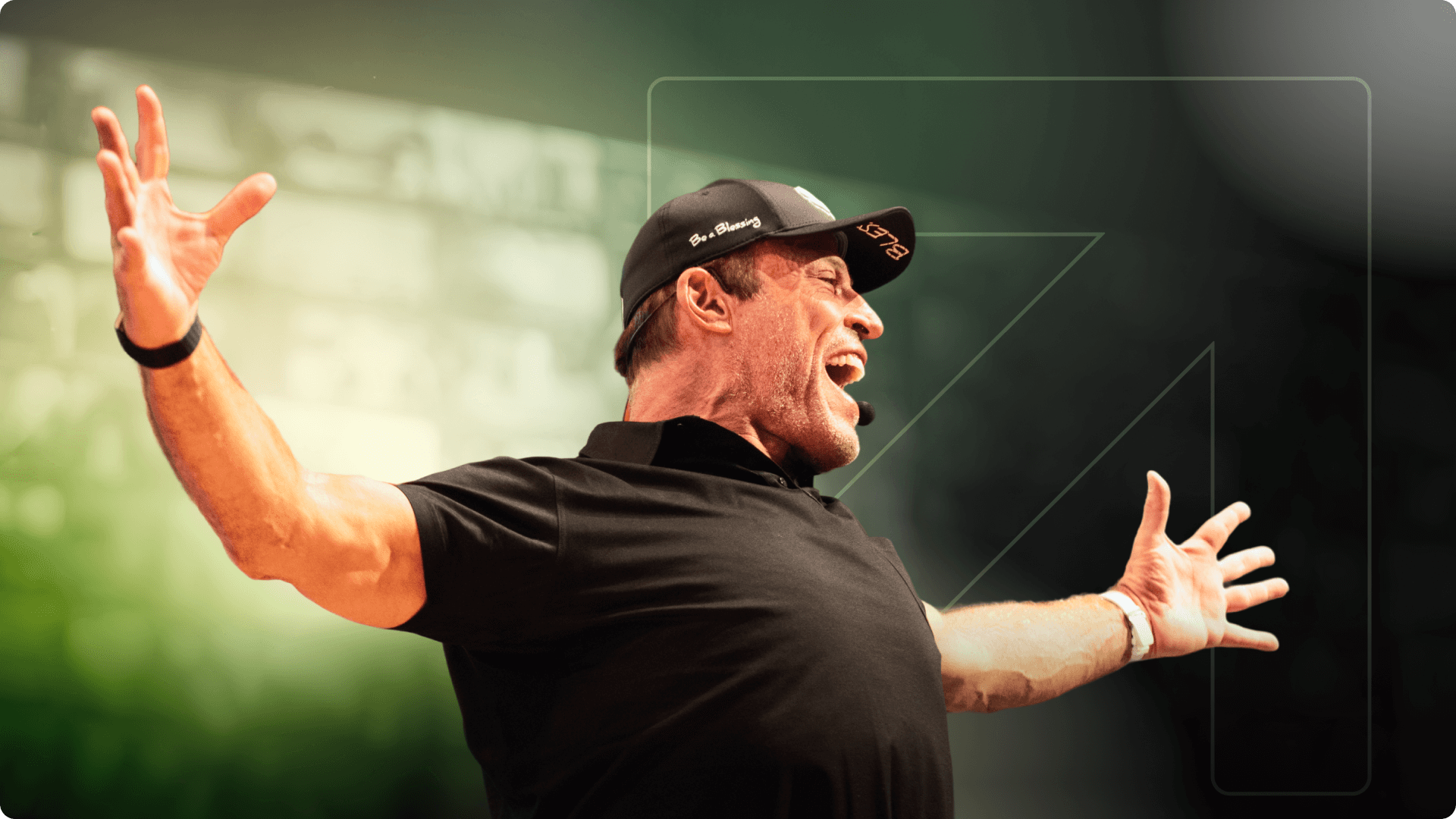 Tony Robbins energetically speaking with arms outstretched, wearing a black cap and shirt.