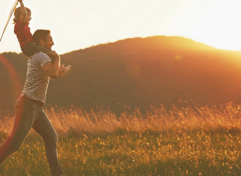 a man is carrying a child on his shoulders in a field at sunset