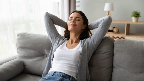 a woman is sitting on a couch with her eyes closed and her hands behind her head .