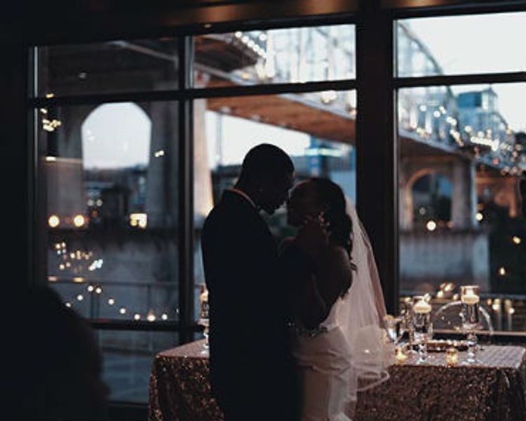 a bride and groom are dancing in front of a window at their wedding reception .