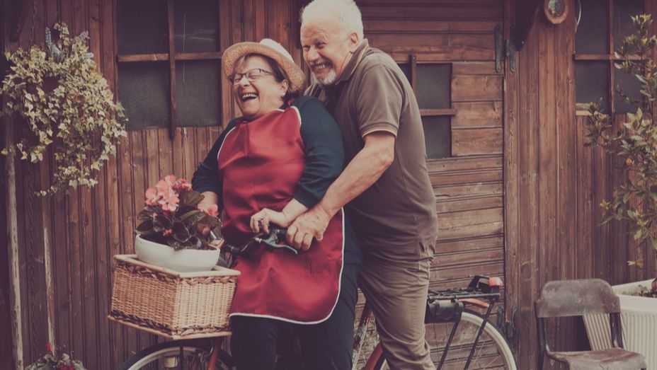 an elderly couple is riding a bicycle in front of a wooden building .