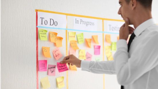 a man is pointing at a board with sticky notes on it .