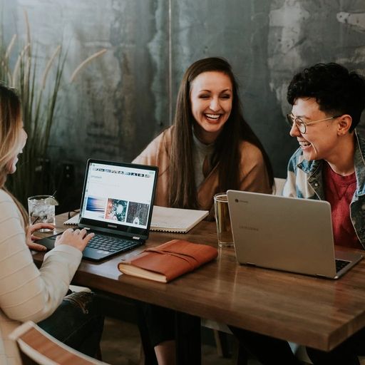 a group of people are sitting at a table with laptops .