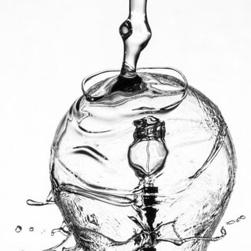 a black and white photo of water pouring into a glass .