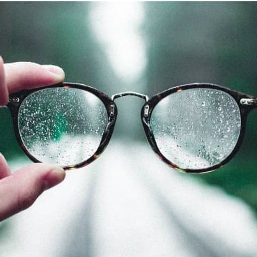a person is holding a pair of glasses with water drops on them .