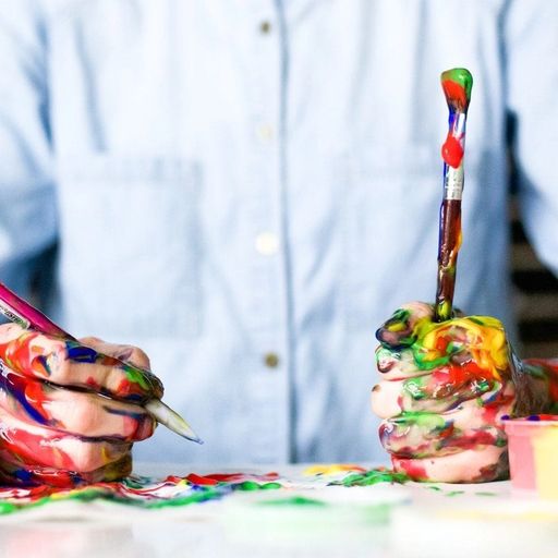 a person is sitting at a table with their hands covered in paint and holding a brush .