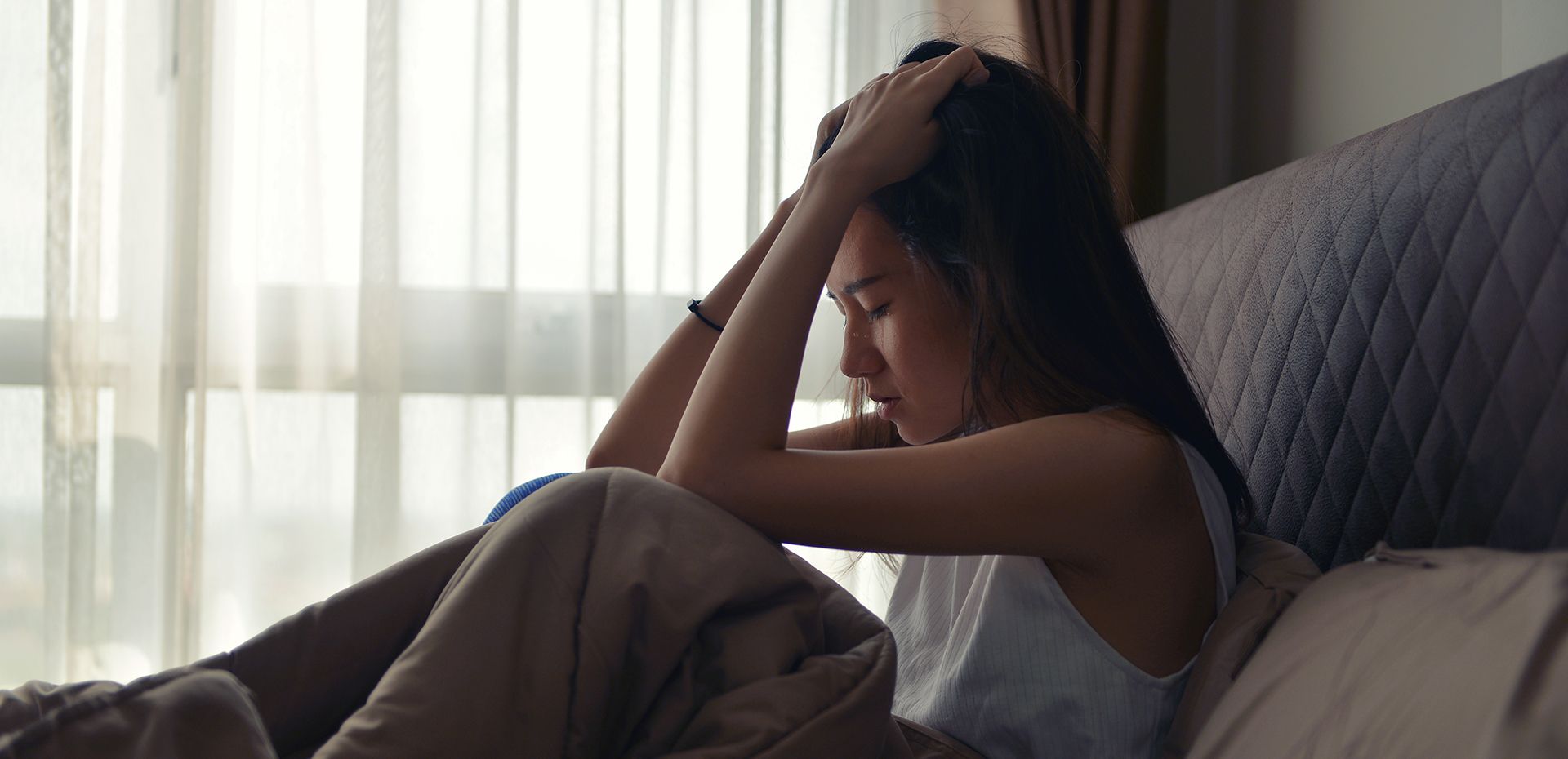 a woman is sitting on a bed with her head in her hands .