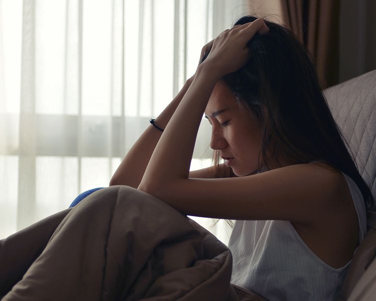 a woman is sitting on a bed with her head in her hands .