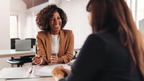 African American Woman smiling across desk at another woman