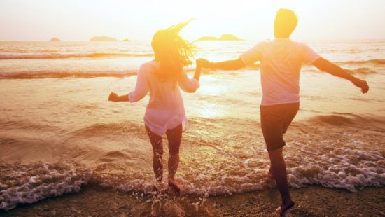 a man and a woman are running on the beach at sunset holding hands .