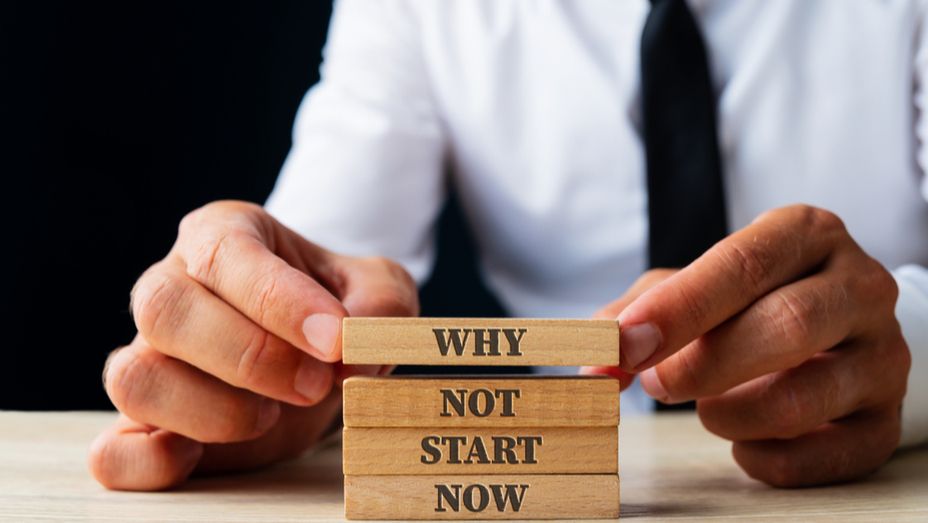 a man is holding wooden blocks with the words `` why not start now '' written on them .