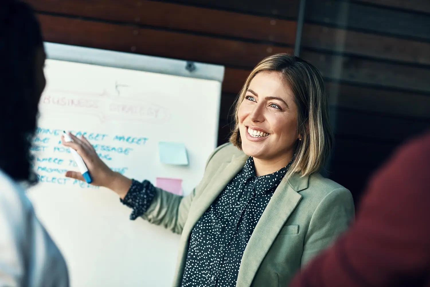 A smiling woman presents a business strategy on a whiteboard.