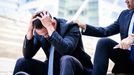 a man in a suit is comforting another man who is sitting on a bench .