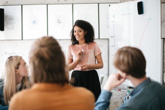a woman is giving a presentation to a group of people in front of a whiteboard .