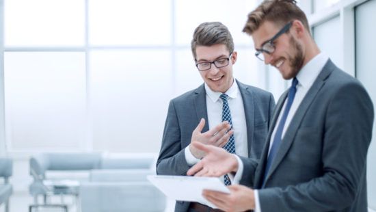 two men in suits and ties are looking at a tablet .