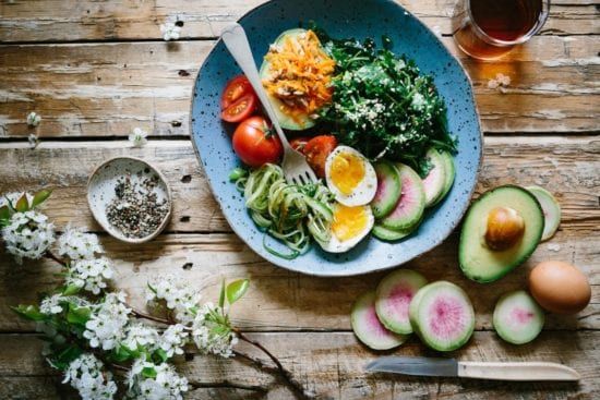 a plate of food with eggs , avocado , and tomatoes on a wooden table .