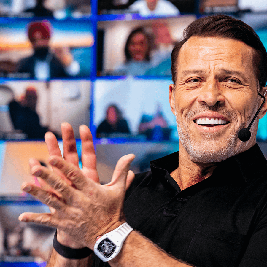 a man wearing a microphone applauds in front of a wall of screens