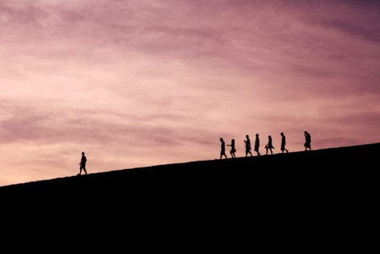 a group of people are walking up a hill at sunset .