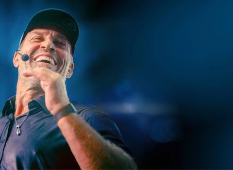 Tony Robbins wearing a hat and a microphone is laughing .