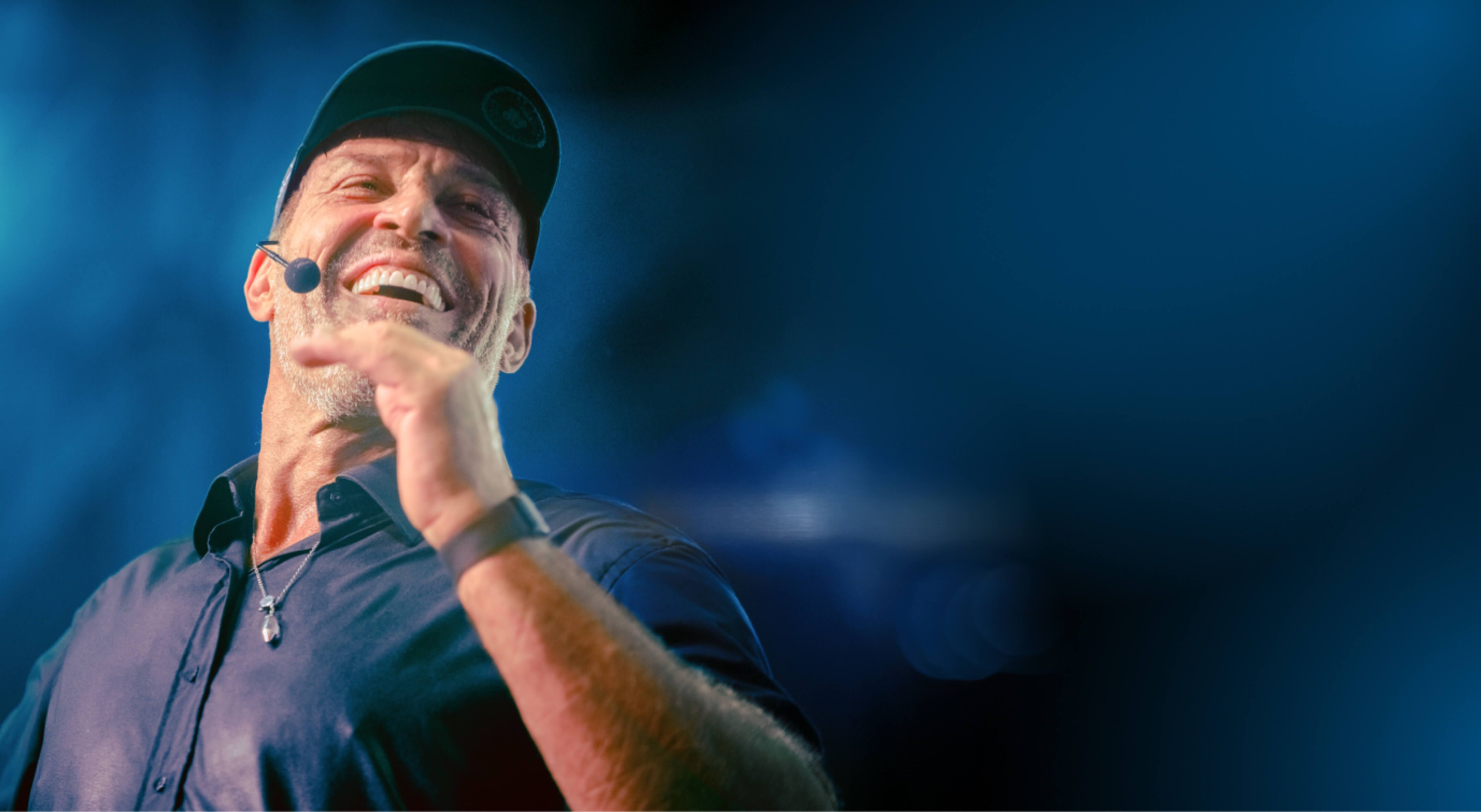 Tony Robbins wearing a hat and a microphone is laughing .