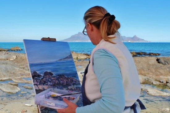 a woman is painting a picture of the ocean on an easel .