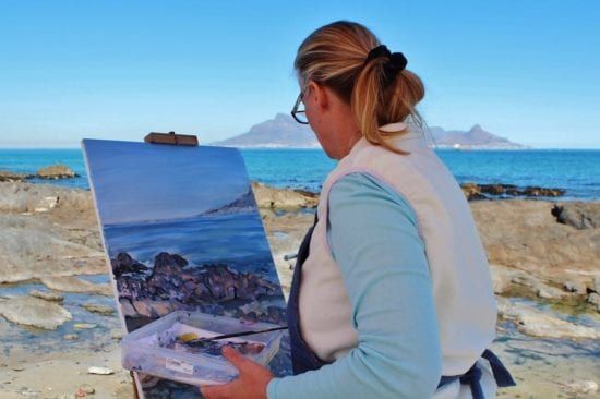 a woman is painting a picture of the ocean on an easel .