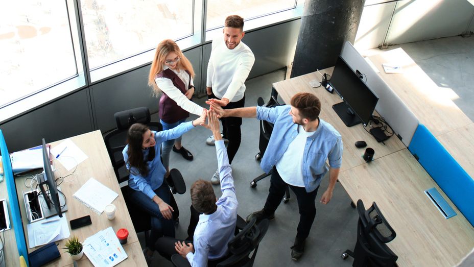 a group of people are giving each other a high five in an office .