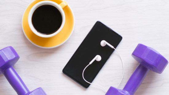 a cup of coffee , a cell phone , headphones , and purple dumbbells on a table .