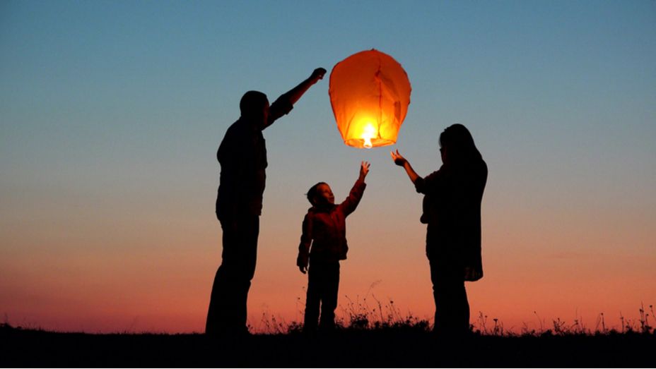 Silhouette of a family releasing a glowing sky lantern at sunset.