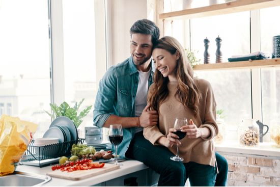 a man and a woman are sitting at a kitchen counter drinking wine .