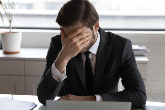 a man in a suit and tie is sitting at a desk with his head in his hands .