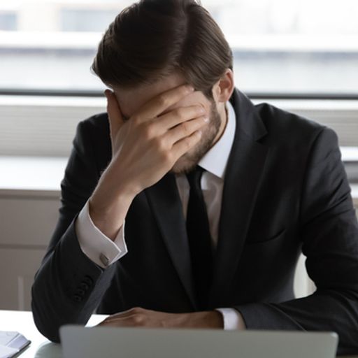a man in a suit and tie is sitting at a desk with his head in his hands .