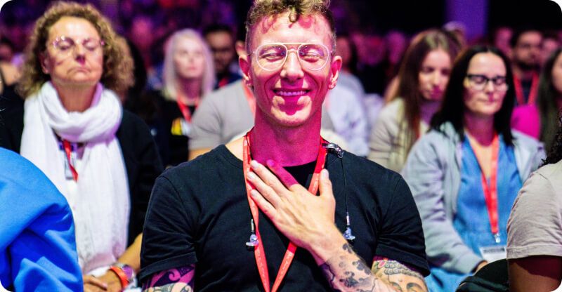 a man is sitting in a crowd of people with his hand on his chest .