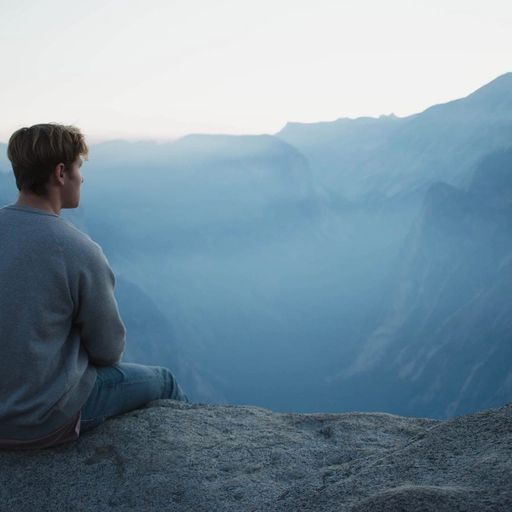 a man is sitting on top of a rock overlooking a mountain range .