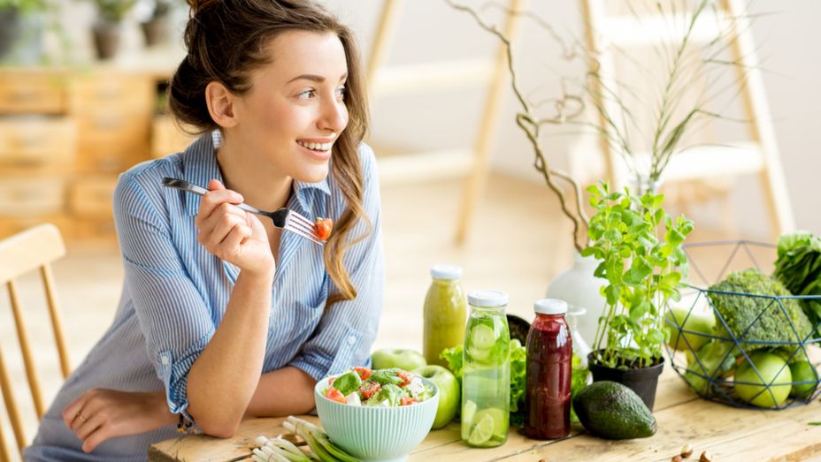 a woman is sitting at a table eating a salad with a fork .