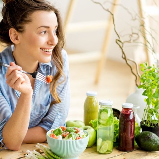 a woman is sitting at a table eating a salad with a fork .
