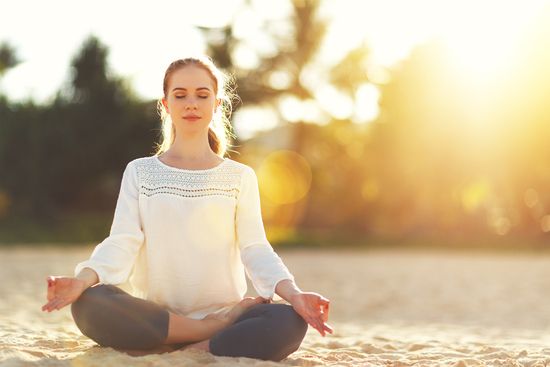 a woman is sitting in a lotus position on the beach with her eyes closed .