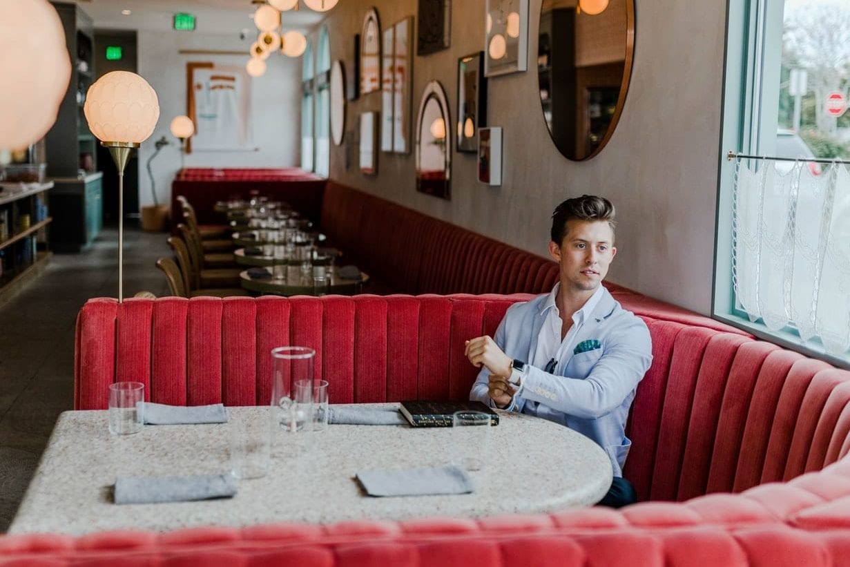 a man is sitting at a table in a restaurant looking at his watch .
