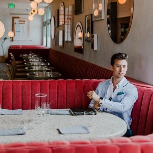 a man is sitting at a table in a restaurant looking at his watch .