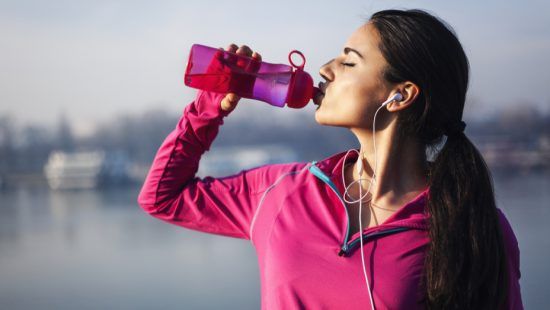 a woman is drinking water from a bottle while listening to music .