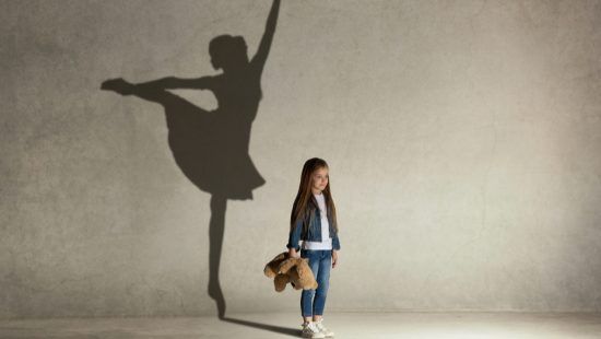 a little girl is standing in front of a wall with a shadow of a ballerina on it .