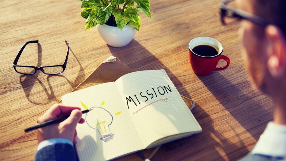 a man is writing in a notebook with the word mission written on it .
