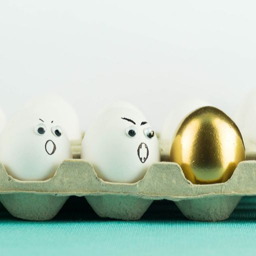 a tray of eggs with faces drawn on them and a gold egg in the middle .